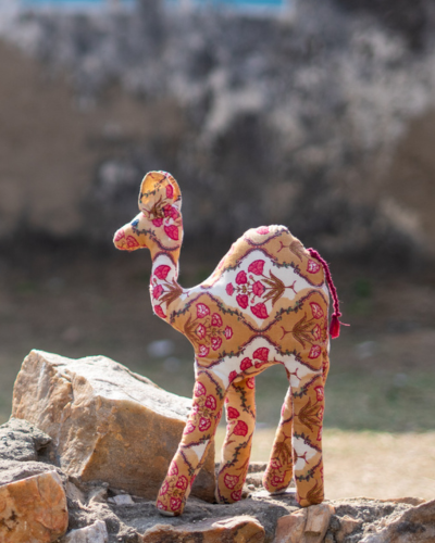 Coco, a handmade floral fabric camel, standing on rocks